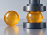 Conceptual CGI: Amber polyurethane sphere shown unloaded beside a second matching sphere under mild broad compression; subtle realistic elastic flattening at contact, no cracks or force values