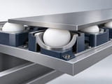Conceptual CGI: Low-load conveyor transfer concept cutaway with a white UHMWPE sphere retained in a broad cup under a flat small metal workpiece; realistic free-rolling contact