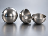 Conceptual CGI: An intact polished stainless sphere alongside a separated hemispherical thin metal shell and matching half-shell; uniform thin wall, visible empty cavity and circumferential joining edge, no solid sphere interior