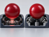 Conceptual CGI: Red optical-patterned resin sphere beside plain red mechanical sphere, each above a simplified optical sensor and roller contact concept respectively; no electronic schematics or text