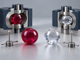 Conceptual CGI: Ruby-red and colourless sapphire solid spheres beside subtle unlabelled crystal-axis orientation fixtures; show corundum colour distinction with polished spherical geometry and no gemstone facets