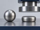 Conceptual CGI: Complete soft steel sphere beside a deliberately flattened same-material sample; forming comparison