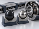Conceptual CGI: Polished dark silicon nitride sphere in an optical inspection cradle with narrow reflected light bands, alongside a silver steel comparison sphere; conceptual surface assessment no digital values