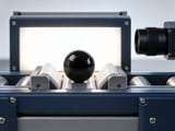 Conceptual CGI: Industrial visual sorting fixture with one black glass sphere against a pale backlit camera inspection background, simple camera lens at edge, no results or numbers