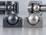 Conceptual CGI: blue-grey tantalum sphere beside pale silver titanium sphere in distinct shallow circular recesses, realistic material comparison with no claimed purity