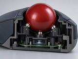 Conceptual CGI: Cutaway industrial trackball module: large red subtly patterned resin sphere resting on three tiny support balls, optical sensor window underneath, compact black enclosure; believable geometry